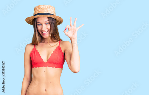 Beautiful brunette young woman wearing bikini smiling positive doing ok sign with hand and fingers. successful expression.