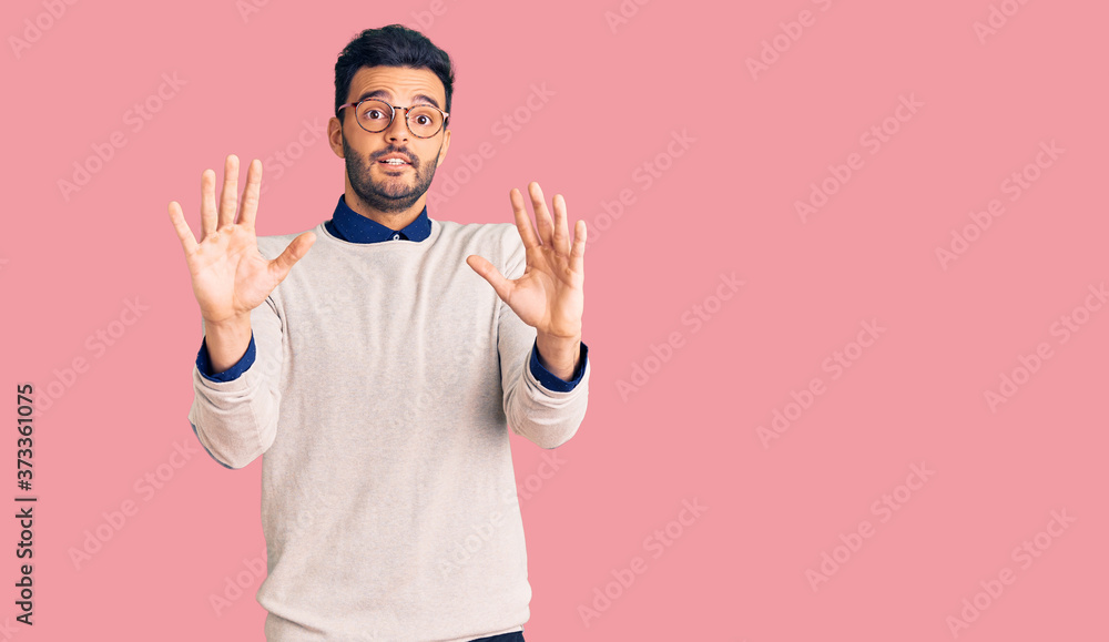 Fototapeta premium Young handsome hispanic man wearing elegant clothes and glasses afraid and terrified with fear expression stop gesture with hands, shouting in shock. panic concept.