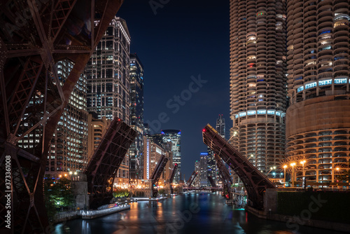 A beautiful long exposure photograph looking down the Chicago River at night as loop bridges along Wacker Drive in downtown are raised up in effort to curb violence and looting and restrict access.
