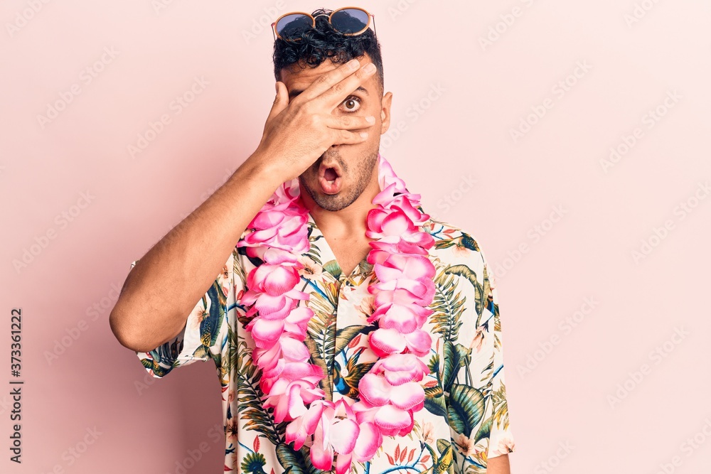 Young hispanic man wearing summer casual clothes peeking in shock covering face and eyes with hand, looking through fingers afraid