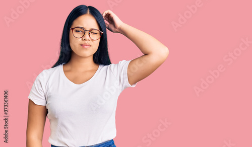 Young beautiful asian girl wearing casual clothes and glasses confuse and wondering about question. uncertain with doubt, thinking with hand on head. pensive concept.