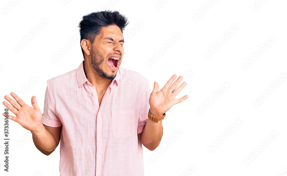 Handsome latin american young man wearing casual summer shirt celebrating mad and crazy for success with arms raised and closed eyes screaming excited. winner concept Handsome latin american young man wearing casual summer shirt celebrating mad and crazy for success with arms raised and closed eyes screaming excited. winner concept