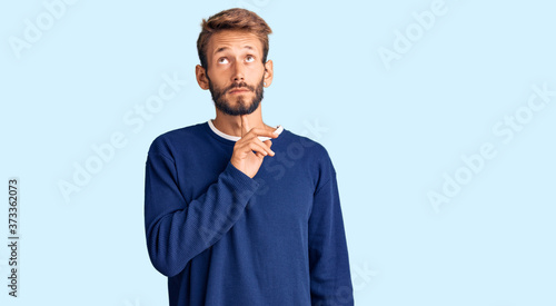 Handsome blond man with beard wearing casual sweater thinking concentrated about doubt with finger on chin and looking up wondering