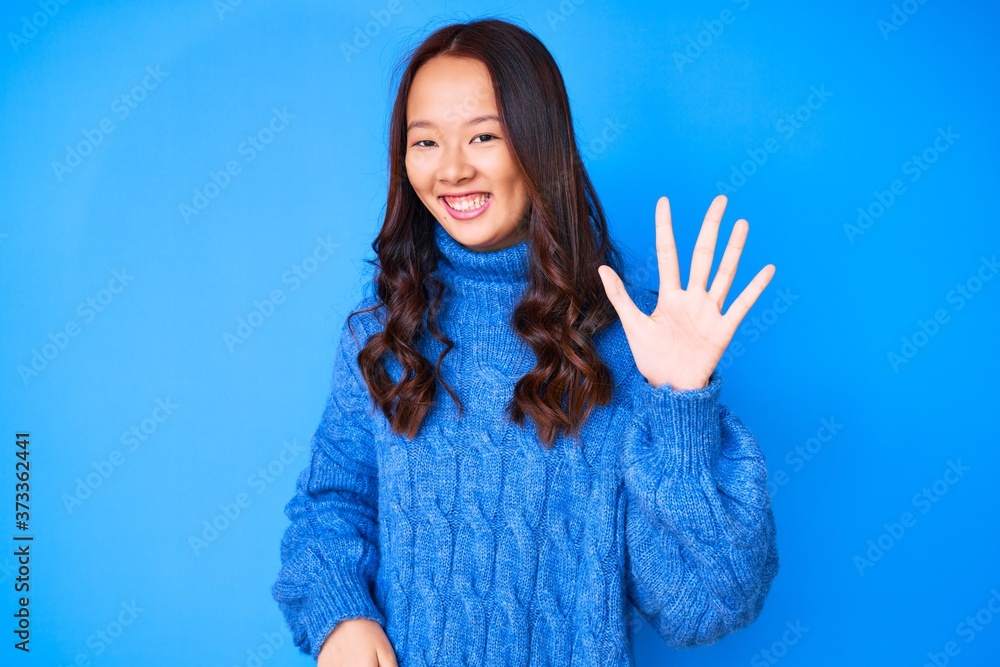 Young beautiful chinese girl wearing casual winter sweater showing and pointing up with fingers number five while smiling confident and happy. Young beautiful chinese girl wearing casual winter sweater showing and pointing up with fingers number five while smiling confident and happy.