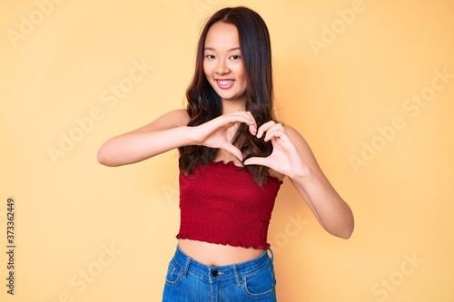 Young beautiful chinese girl wearing summer clothes smiling in love showing heart symbol and shape with hands. romantic concept.