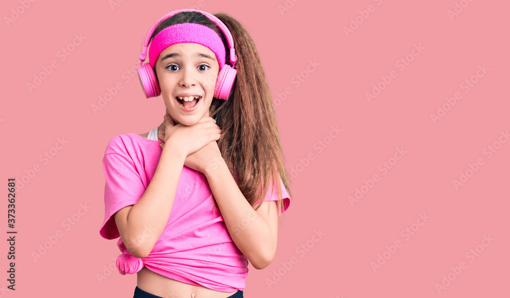 Cute hispanic child girl wearing gym clothes and using headphones shouting and suffocate because painful strangle. health problem. asphyxiate and suicide concept. Cute hispanic child girl wearing gym clothes and using headphones shouting and suffocate because painful strangle. health problem. asphyxiate and suicide concept.