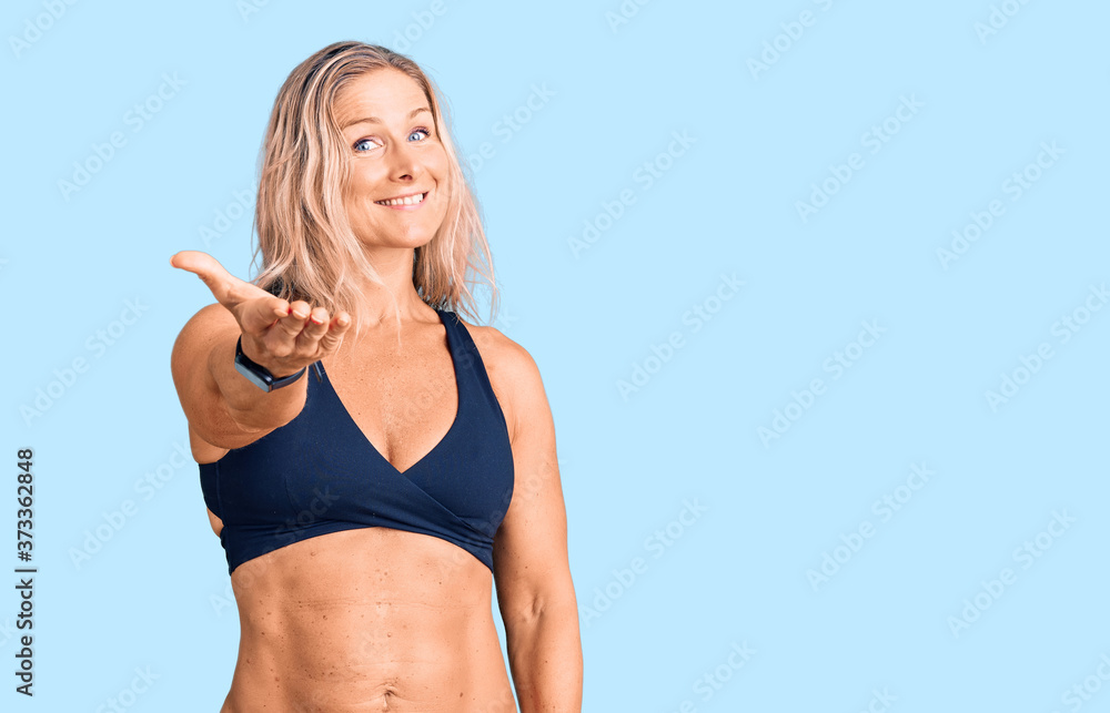 Middle age fit blonde woman wearing bikini smiling friendly offering handshake as greeting and welcoming. successful business. Middle age fit blonde woman wearing bikini smiling friendly offering handshake as greeting and welcoming. successful business.