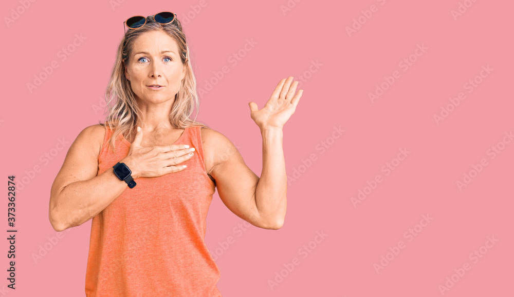 Middle age fit blonde woman wearing casual summer clothes and sunglasses swearing with hand on chest and open palm, making a loyalty promise oath Middle age fit blonde woman wearing casual summer clothes and sunglasses swearing with hand on chest and open palm, making a loyalty promise oath