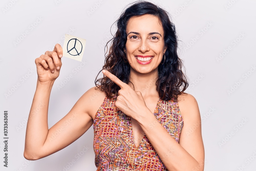 Young beautiful hispanic woman holding peace symbol reminder paper smiling happy pointing with hand and finger Young beautiful hispanic woman holding peace symbol reminder paper smiling happy pointing with hand and finger