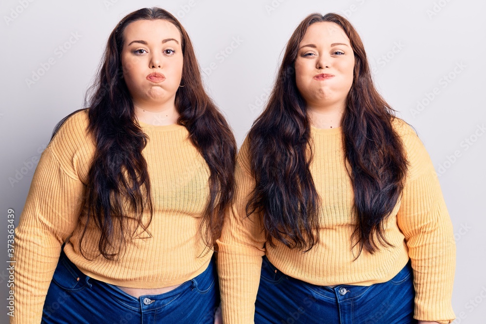 Young plus size twins wearing casual clothes puffing cheeks with funny face. mouth inflated with air, crazy expression. Young plus size twins wearing casual clothes puffing cheeks with funny face. mouth inflated with air, crazy expression.