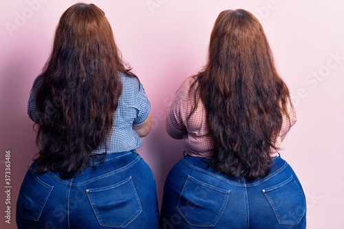 Young plus size twins wearing casual clothes standing backwards looking away with crossed arms