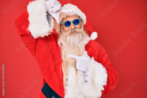 Old senior man wearing santa claus costume and sunglasses smiling making frame with hands and fingers with happy face. creativity and photography concept.