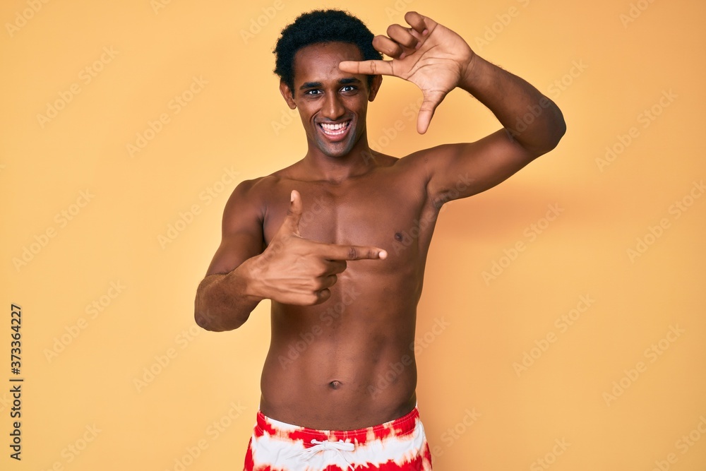 African handsome man wearing swimsuit smiling making frame with hands and fingers with happy face. creativity and photography concept.