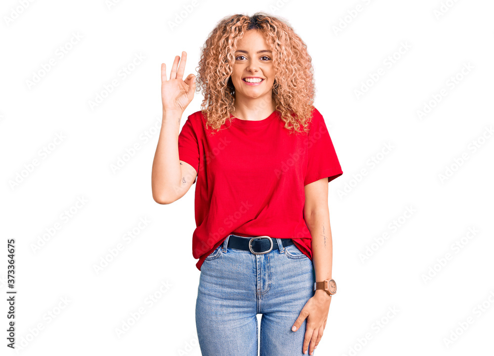 Young blonde woman with curly hair wearing casual red tshirt smiling positive doing ok sign with hand and fingers. successful expression.