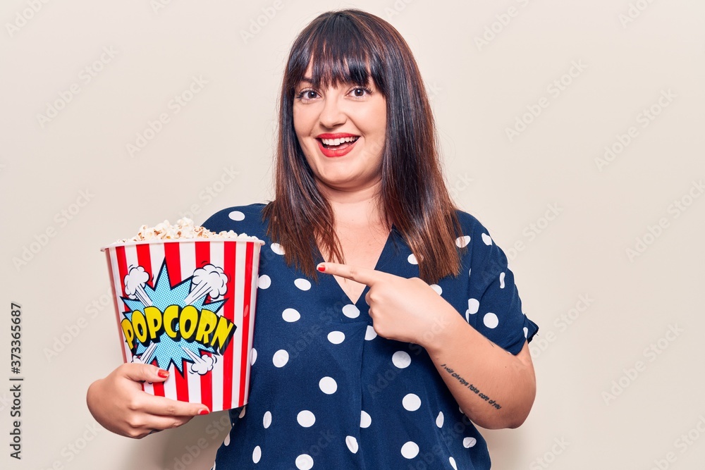 Young plus size woman holding popcorn smiling happy pointing with hand and finger Young plus size woman holding popcorn smiling happy pointing with hand and finger
