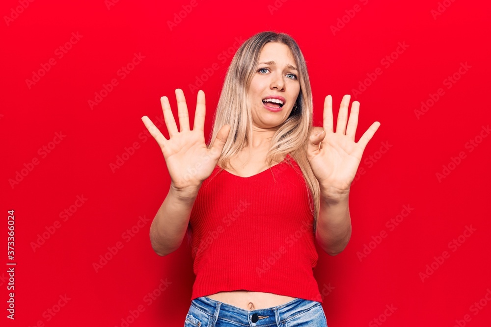 Young blonde woman wearing casual clothes afraid and terrified with fear expression stop gesture with hands, shouting in shock. panic concept. Young blonde woman wearing casual clothes afraid and terrified with fear expression stop gesture with hands, shouting in shock. panic concept.
