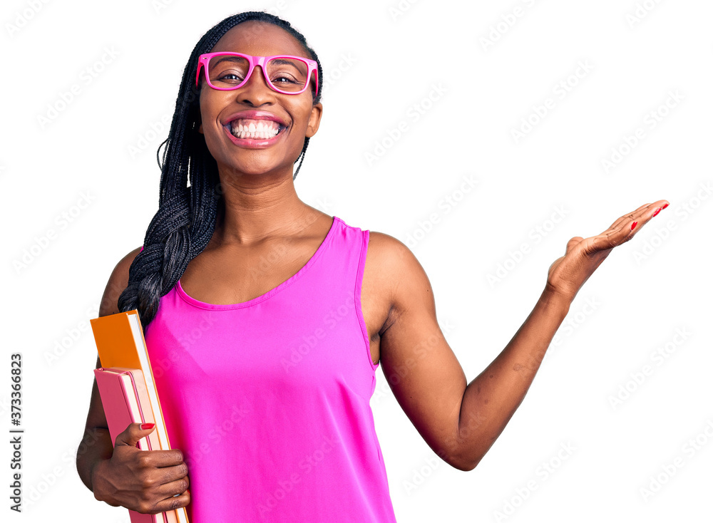 Young african american woman wearing glasses holding book celebrating victory with happy smile and winner expression with raised hands Young african american woman wearing glasses holding book celebrating victory with happy smile and winner expression with raised hands