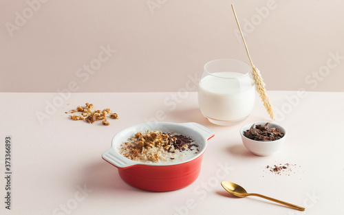 Oatmeal porridge with nuts, chocolate on a soft pink background. Food styling, trends in food photography. Good morning.