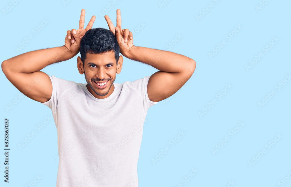 Young latin man wearing casual clothes posing funny and crazy with fingers on head as bunny ears, smiling cheerful Young latin man wearing casual clothes posing funny and crazy with fingers on head as bunny ears, smiling cheerful
