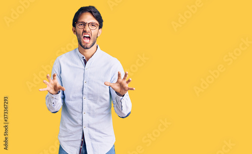 Handsome hispanic man wearing business shirt and glasses smiling funny doing claw gesture as cat, aggressive and sexy expression