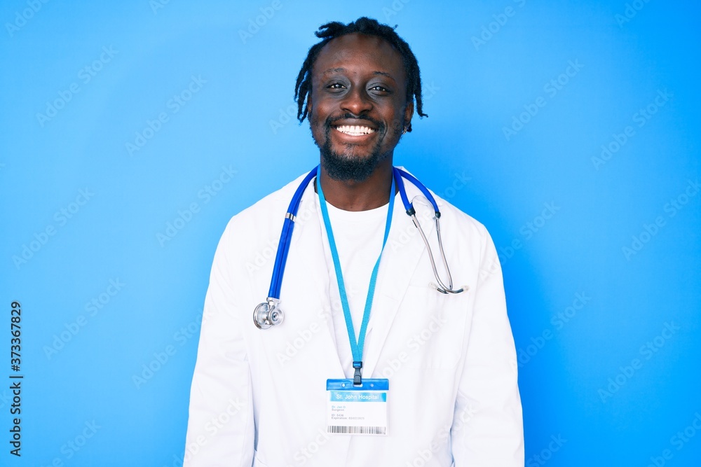 Young african american man with braids wearing doctor stethoscope and id pass looking positive and happy standing and smiling with a confident smile showing teeth Young african american man with braids wearing doctor stethoscope and id pass looking positive and happy standing and smiling with a confident smile showing teeth