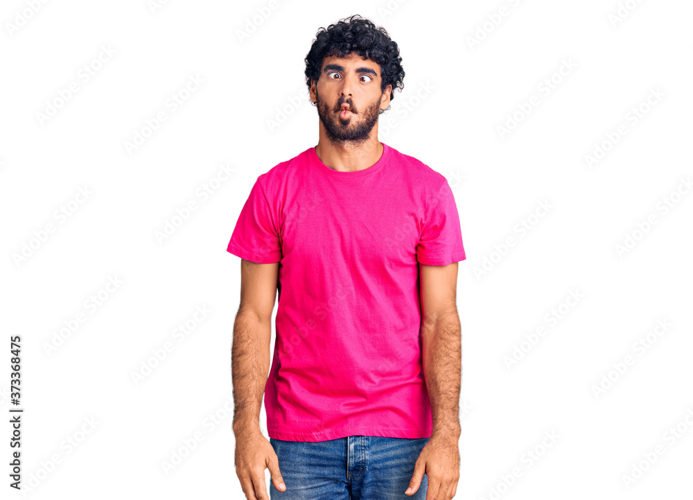 Handsome young man with curly hair and bear wearing casual pink tshirt making fish face with lips, crazy and comical gesture. funny expression. Handsome young man with curly hair and bear wearing casual pink tshirt making fish face with lips, crazy and comical gesture. funny expression.