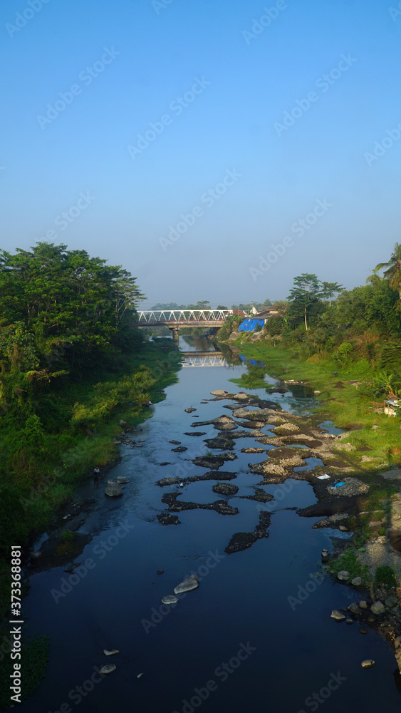 Sunny morning on the Pabelan River. Clear river water, green trees, blue sky and a bridge in the distance Sunny morning on the Pabelan River. Clear river water, green trees, blue sky and a bridge in the distance