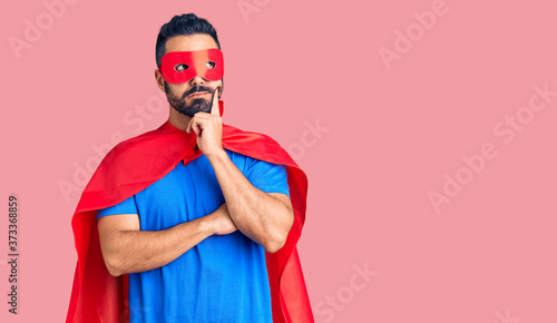 Young hispanic man wearing super hero costume serious face thinking about question with hand on chin, thoughtful about confusing idea © Krakenimages.com