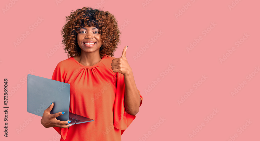 Young african american woman working using computer laptop smiling happy and positive, thumb up doing excellent and approval sign Young african american woman working using computer laptop smiling happy and positive, thumb up doing excellent and approval sign