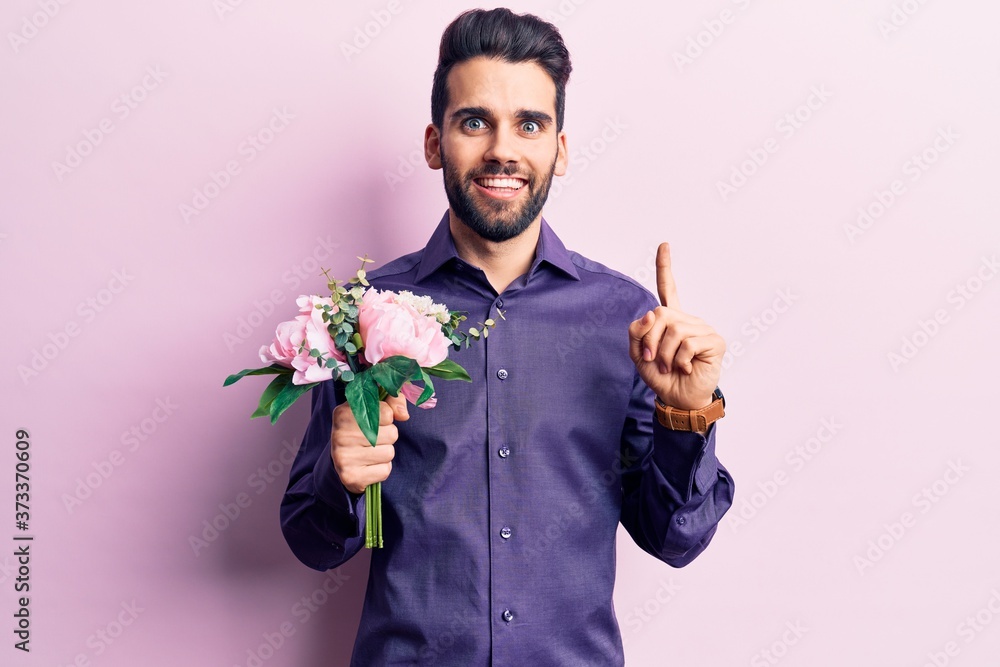 Young handsome man with beard holding bouquet of flowers smiling with an idea or question pointing finger with happy face, number one Young handsome man with beard holding bouquet of flowers smiling with an idea or question pointing finger with happy face, number one