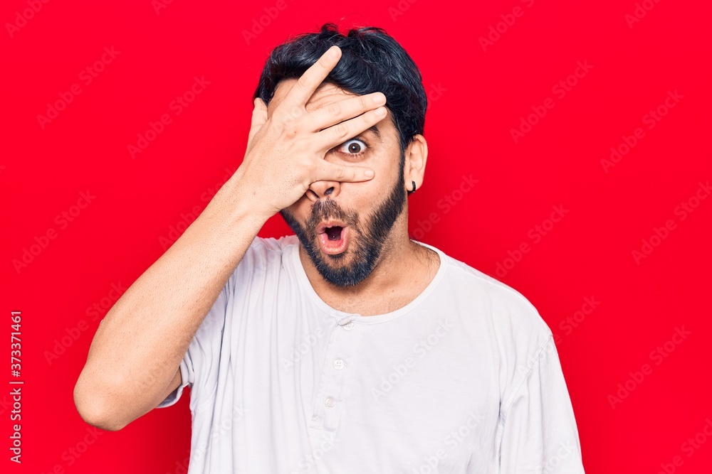 Young hispanic man wearing casual clothes peeking in shock covering face and eyes with hand, looking through fingers afraid Young hispanic man wearing casual clothes peeking in shock covering face and eyes with hand, looking through fingers afraid