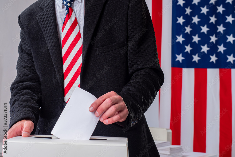 Voting box in USA. Voting president USA. Voter throws bill into election box. Man at polling station in United States. Man next to election box. Ballot urn next America flags. Presidential elections. Voting box in USA. Voting president USA. Voter throws bill into election box. Man at polling station in United States. Man next to election box. Ballot urn next America flags. Presidential elections.