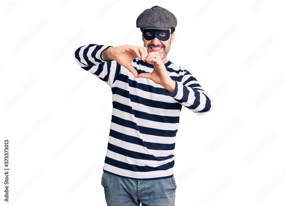 Middle age handsome man wearing burglar mask smiling in love doing heart symbol shape with hands. romantic concept. Middle age handsome man wearing burglar mask smiling in love doing heart symbol shape with hands. romantic concept.