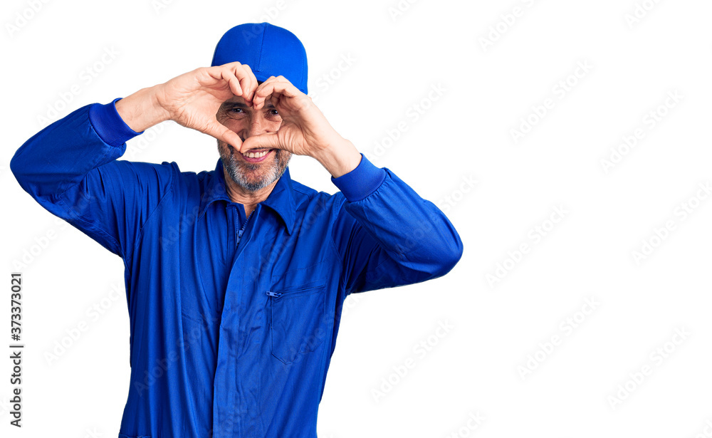 Naklejka premium Middle age handsome man wearing mechanic uniform doing heart shape with hand and fingers smiling looking through sign