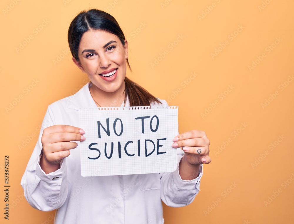 Young beautiful brunette psychologist woman holding paper with not to suicide message looking positive and happy standing and smiling with a confident smile showing teeth Young beautiful brunette psychologist woman holding paper with not to suicide message looking positive and happy standing and smiling with a confident smile showing teeth