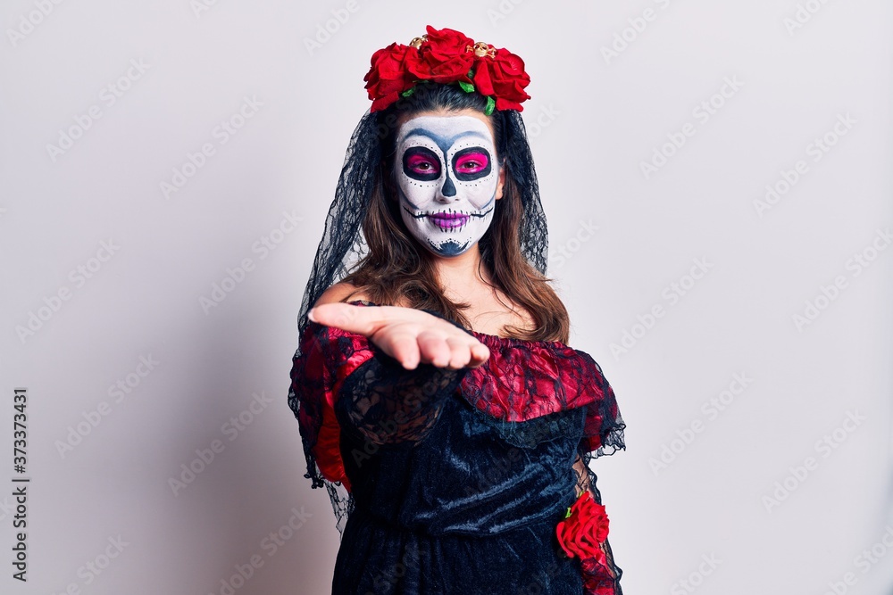Young woman wearing day of the dead costume over white smiling cheerful offering palm hand giving assistance and acceptance.
