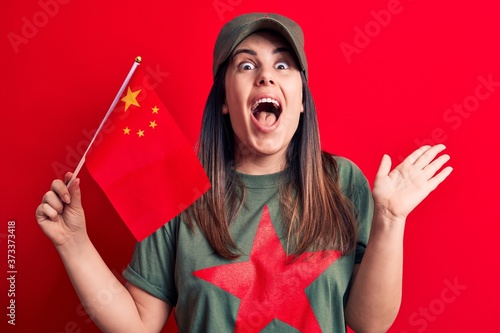 Beautiful patriotic woman wearing t-shirt with red star communist symbol holding china flag celebrating achievement with happy smile and winner expression with raised hand photo