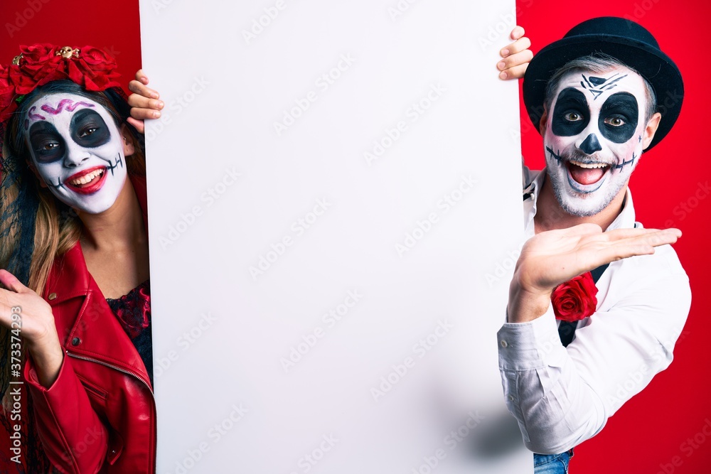 Couple wearing day of the dead costume holding blank empty banner celebrating victory with happy smile and winner expression with raised hands Couple wearing day of the dead costume holding blank empty banner celebrating victory with happy smile and winner expression with raised hands