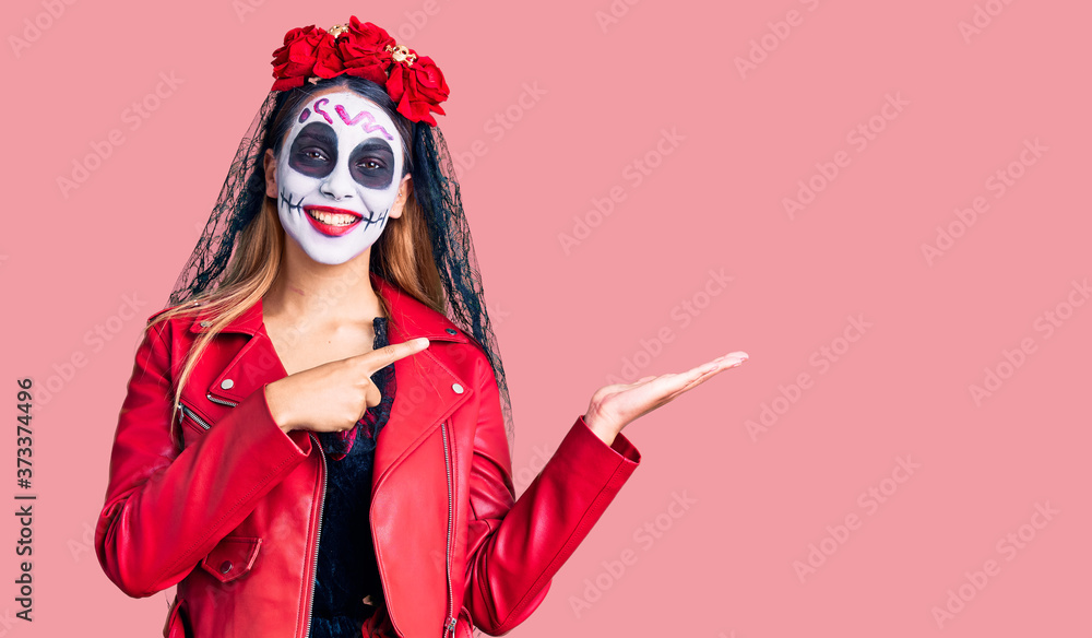 Woman wearing day of the dead costume over background amazed and smiling to the camera while presenting with hand and pointing with finger.