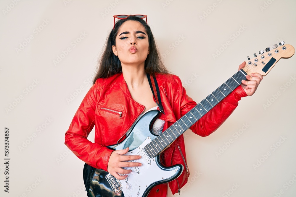 Brunette teenager girl playing electric guitar looking at the camera blowing a kiss being lovely and sexy. love expression. Brunette teenager girl playing electric guitar looking at the camera blowing a kiss being lovely and sexy. love expression.