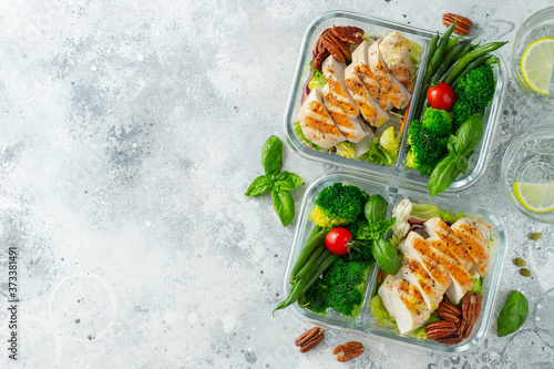 Healthy meal prep containers with green beans, chicken breast and broccoli. A set of food for keto diet in lunchbox on a light concrete background. Top view with copy space