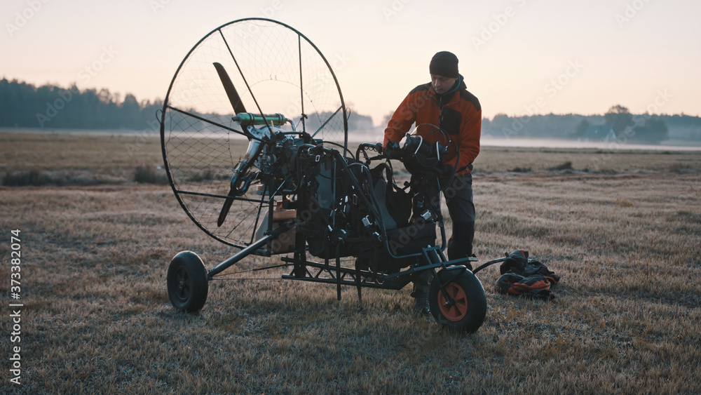 Obraz premium Tandem paramotorgliding. Man in standing near the paramotor during the sunset. High quality photo