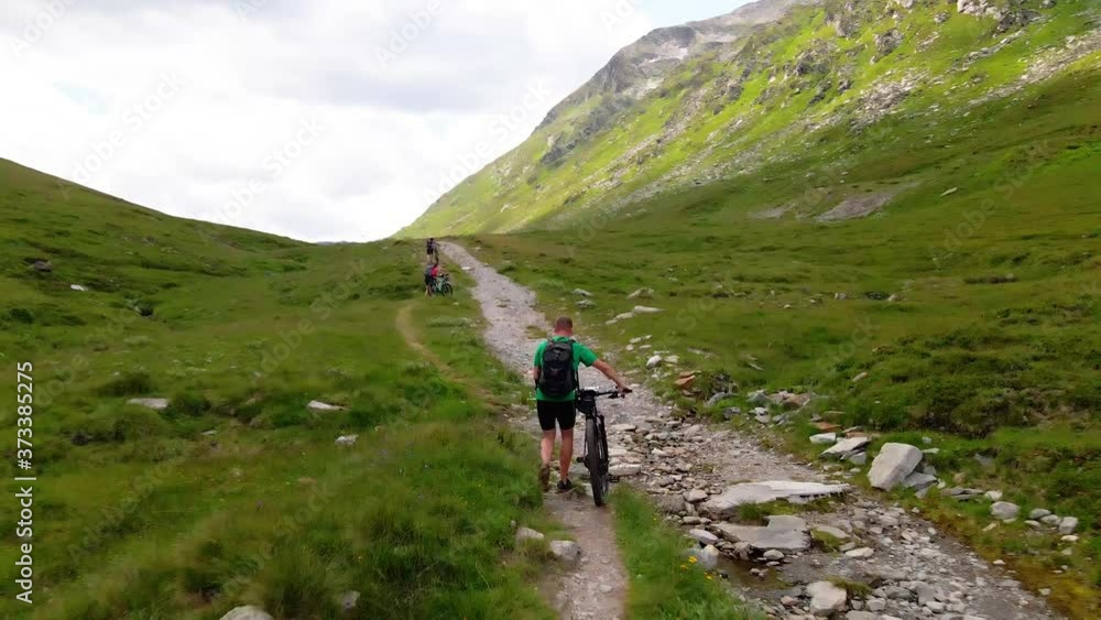 Three mountainbikers pushing up their bikes on a steep track in the Alps. Three mountainbikers pushing up their bikes on a steep track in the Alps.