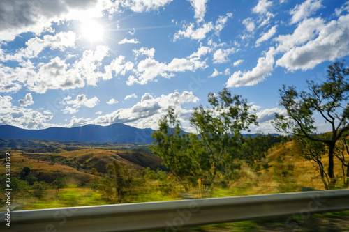 Fotografi Motion blur in the foreground of a beautiful rural landscape with distant mountains, blue sky with clouds, and late afternoon sun