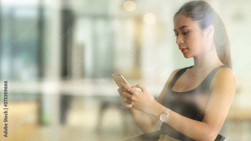View through glass window of female texting on smartphone in office room