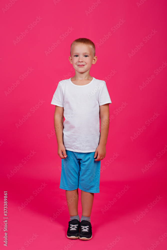 A cute 5-year-old boy in a white t-shirt and blue shorts. Full growth. Pink background. Vertical. A cute 5-year-old boy in a white t-shirt and blue shorts. Full growth. Pink background. Vertical.