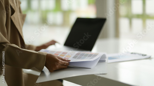 Side view of female designer choosing colour while working with laptop