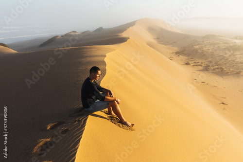 Man enjoying sunrise on top of huge sand dune. Beautiful warm sun light. Sahara desert, Morocco.