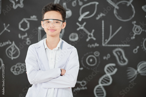 Portrait of happy little Vietnamese boy in labcoat and goggles crossing arms and looking at camera