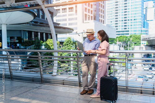 tourist older woman and man wearing casual dress   hand holding baggage for travel walking and talking passed the public sky walk bridge.